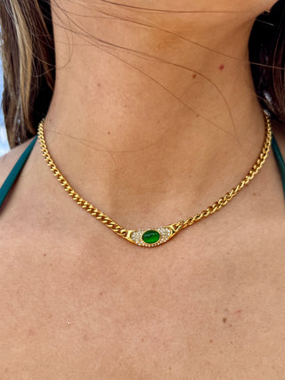 Gold chain necklace with a green gemstone and clear stones on a person's neck.