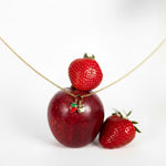 Nadare Co. Apple Charm and strawberry charm on a gold chain draped over a fresh red apple and strawberries.