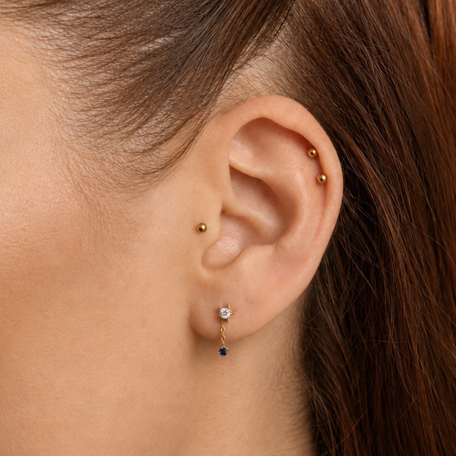 Nadare Co. Astra threadless earring featuring a gold star with clear CZ and a sapphire blue drop on a delicate chain.
