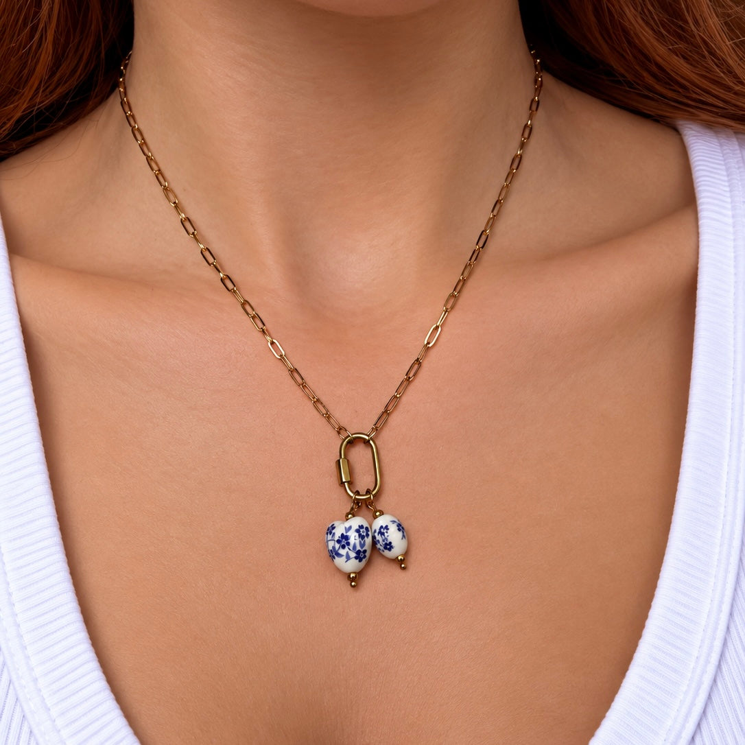 Nadare Co. gold chain necklace featuring two blue floral porcelain heart charms with 14k gold plated accents.