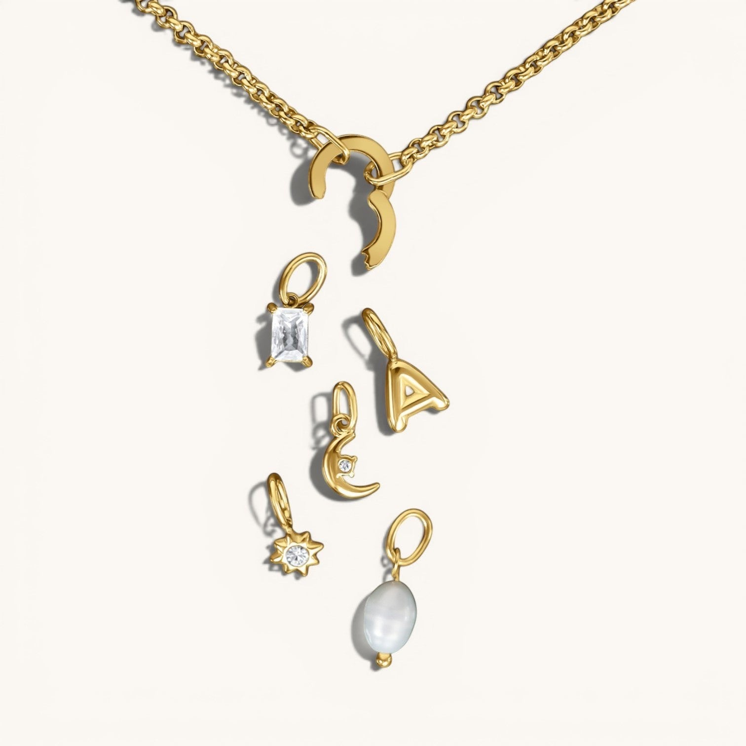 Nadare Co. customizable gold chain necklace with a clasp and various charms including a pearl, letter, and crystals.