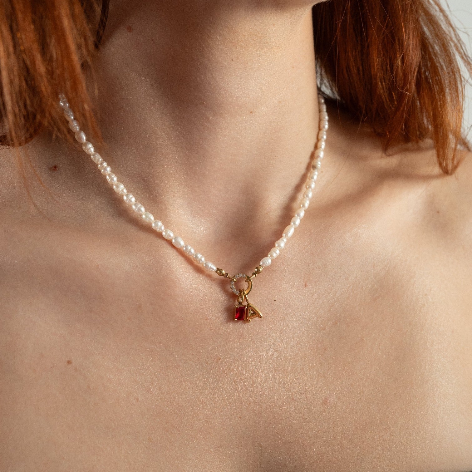Nadare Co. freshwater pearl necklace featuring a gold clasp with a red gemstone charm worn on a woman's neck.
