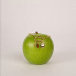 Nadare Co. gold apple charm with a letter a and red bead charm on a gold chain resting on a fresh green apple.