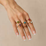 Nadare Co. gold birthstone rings featuring vibrant colorful gemstones worn on a woman's hand with a French manicure.