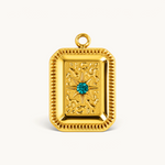 Nadare Co. gold rectangular tablet charm with textured detailing and a central emerald green cubic zirconia stone.
