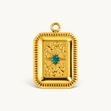 Nadare Co. gold rectangular tablet charm with textured detailing and a central emerald green cubic zirconia stone.