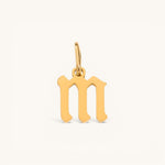 Nadare Co. gold-plated stainless steel gothic letter M charm with sharp edges on a plain background