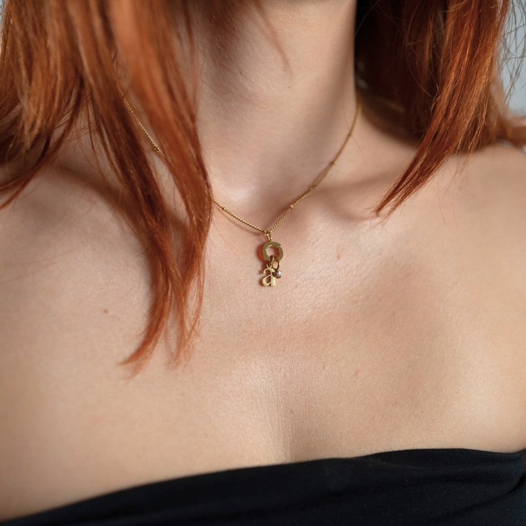 Nadare Co. gold initial and mini birthstone pendant necklace worn on a woman with red hair