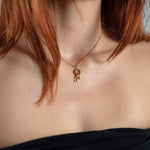 Nadare Co. gold initial and mini birthstone pendant necklace worn on a woman with red hair