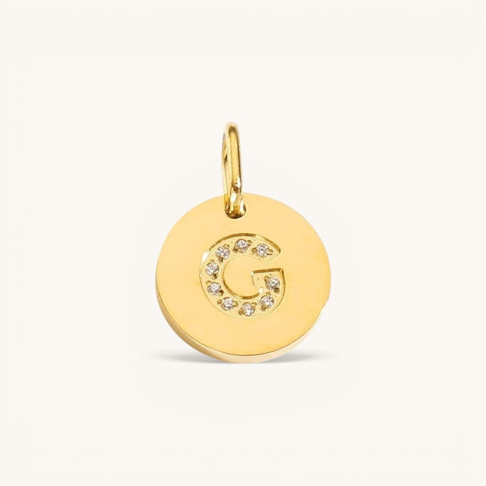 Nadare Co. gold initial G charm with pavé set diamonds on a polished disc.