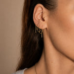 Nadare Co. gold chain threader earrings worn in multiple ear piercings, featuring delicate dangling bar charms.