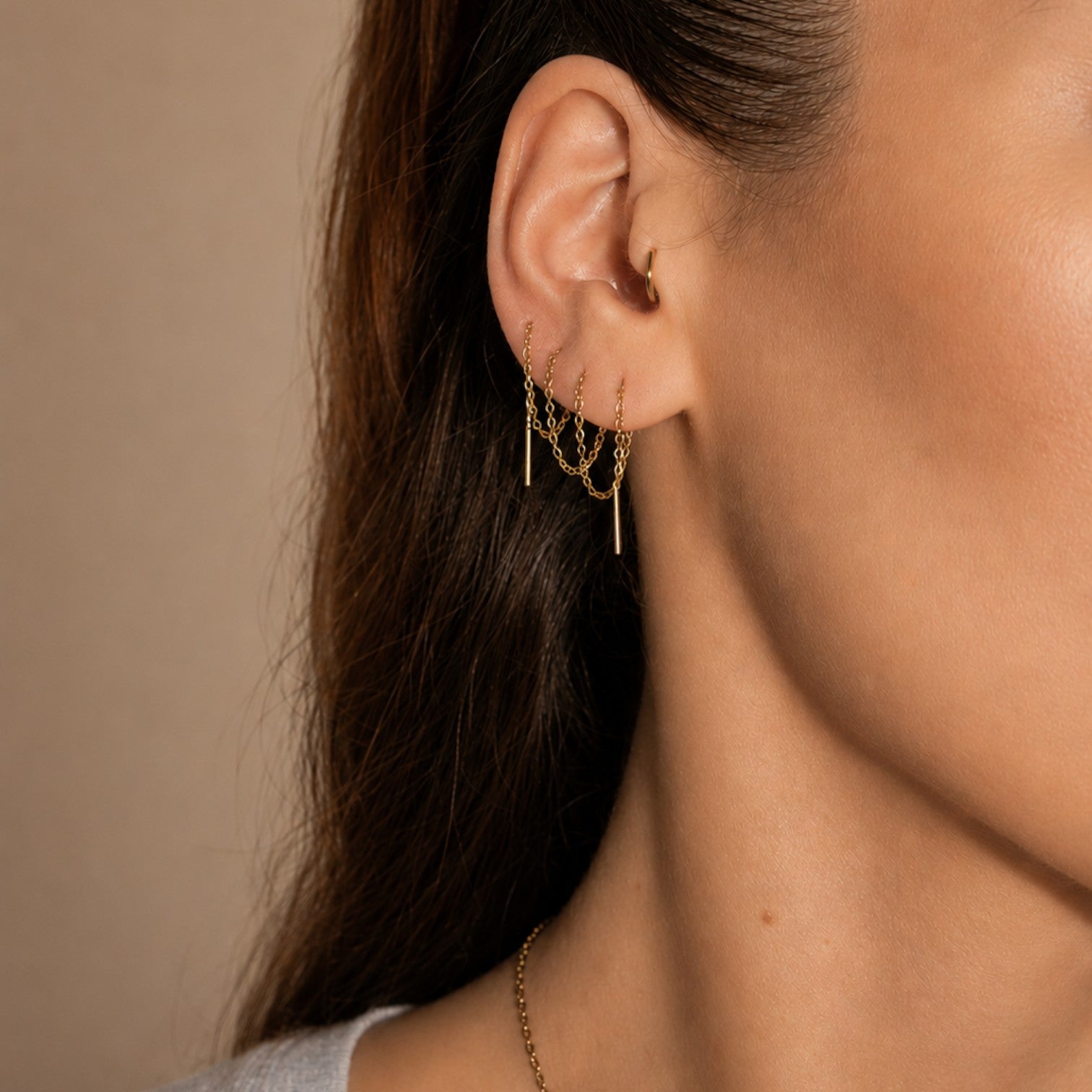 Nadare Co. gold chain threader earrings worn in multiple ear piercings, featuring delicate dangling bar charms.