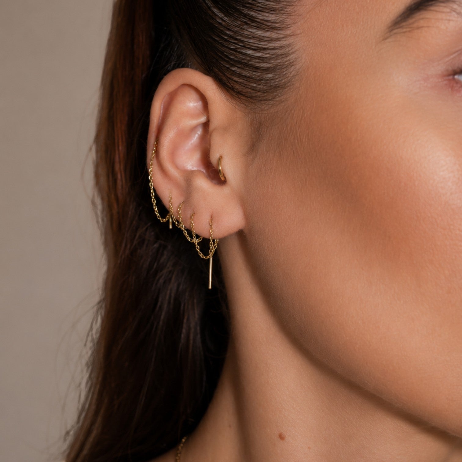Nadare Co. gold chain threader earrings worn in multiple ear piercings on a woman's ear