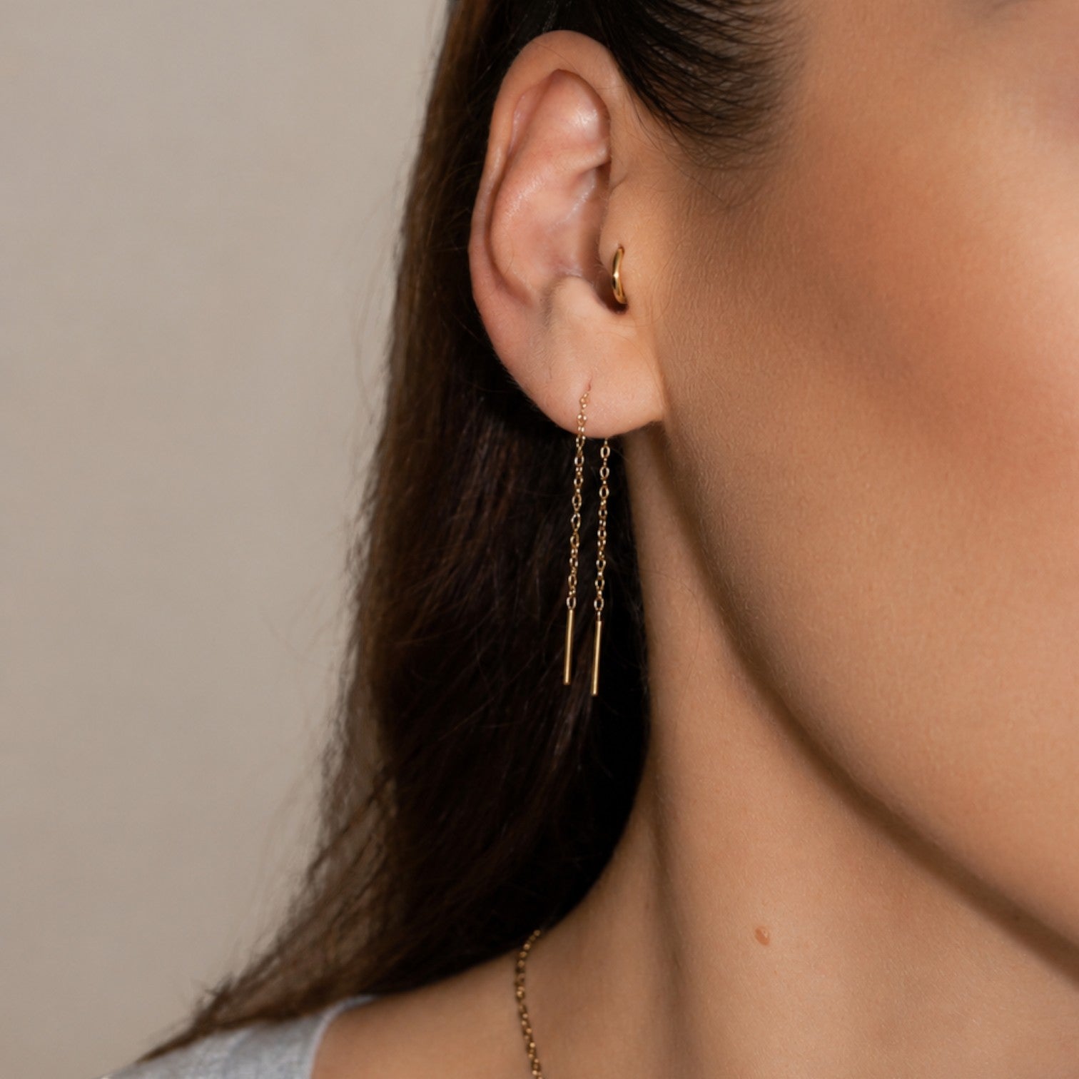 Nadare Co. gold threader earrings worn on a woman's earlobe with a small gold hoop in the tragus