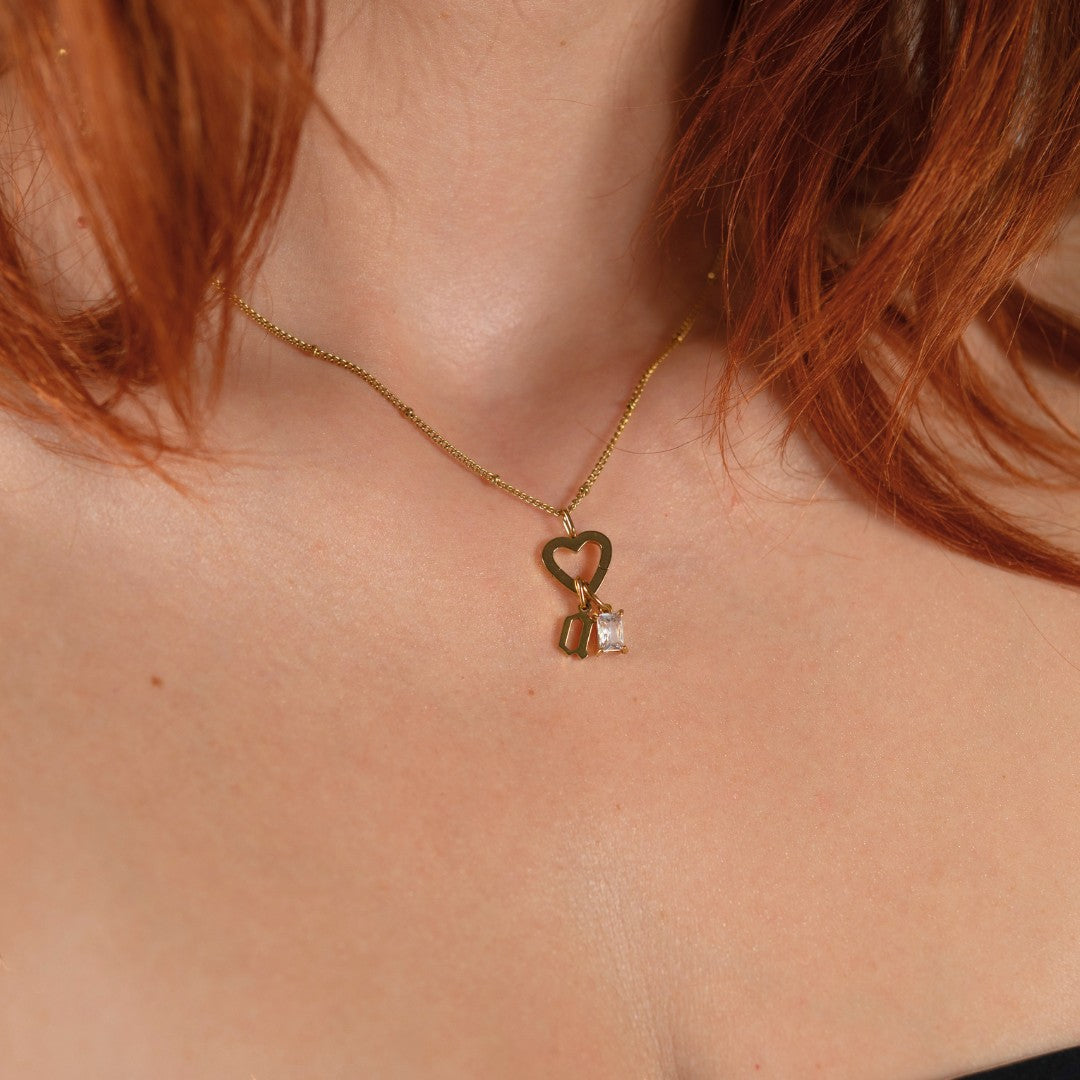 Nadare Co. gold gothic initial necklace with a heart charm and clear birthstone worn on a woman's neck