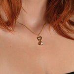 Nadare Co. gold gothic initial necklace with a heart charm and clear birthstone worn on a woman's neck
