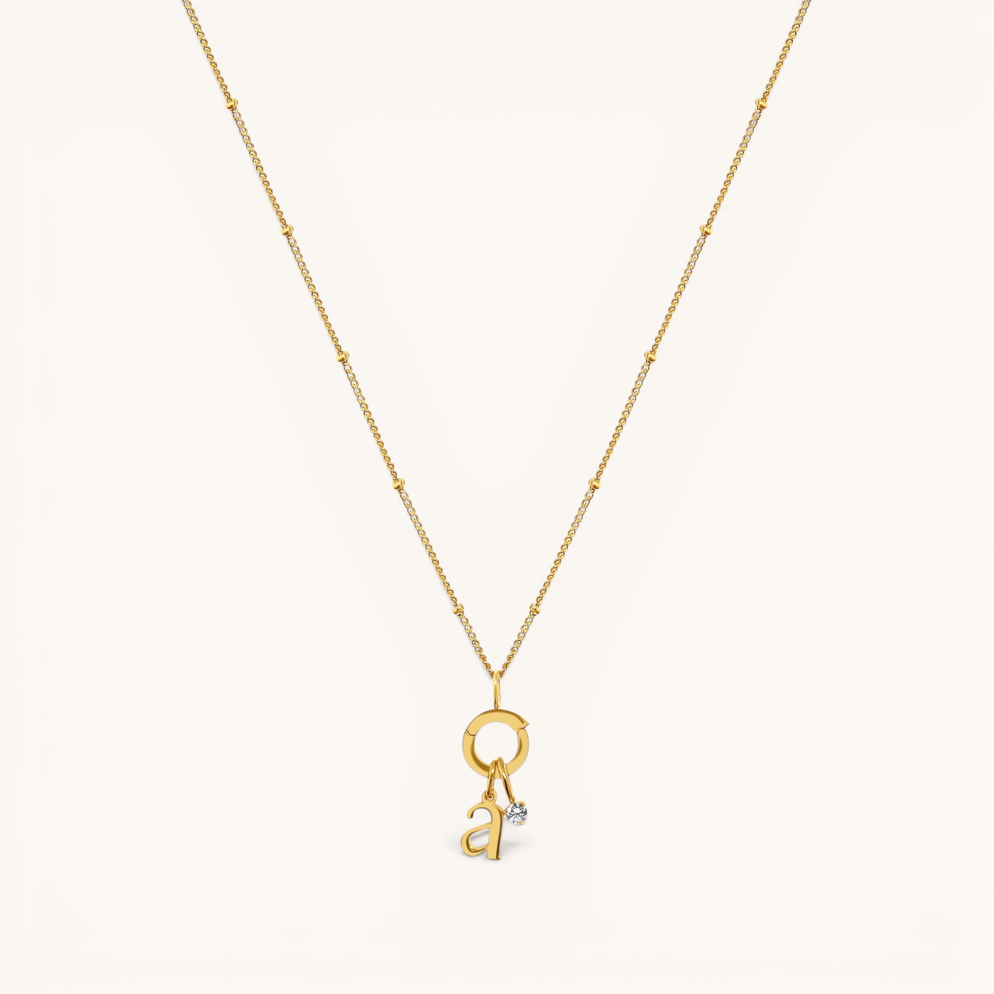 Nadare Co. gold chain necklace featuring a delicate letter a initial charm and a small sparkling birthstone pendant