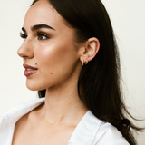 Model wearing Nadare Co. Livia Huggies, 18k gold-plated stainless steel hoop earrings in a minimalist style.