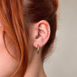 Nadare Co. Lola Hoops in polished gold stainless steel worn on a woman with red hair, showing a classic round design.