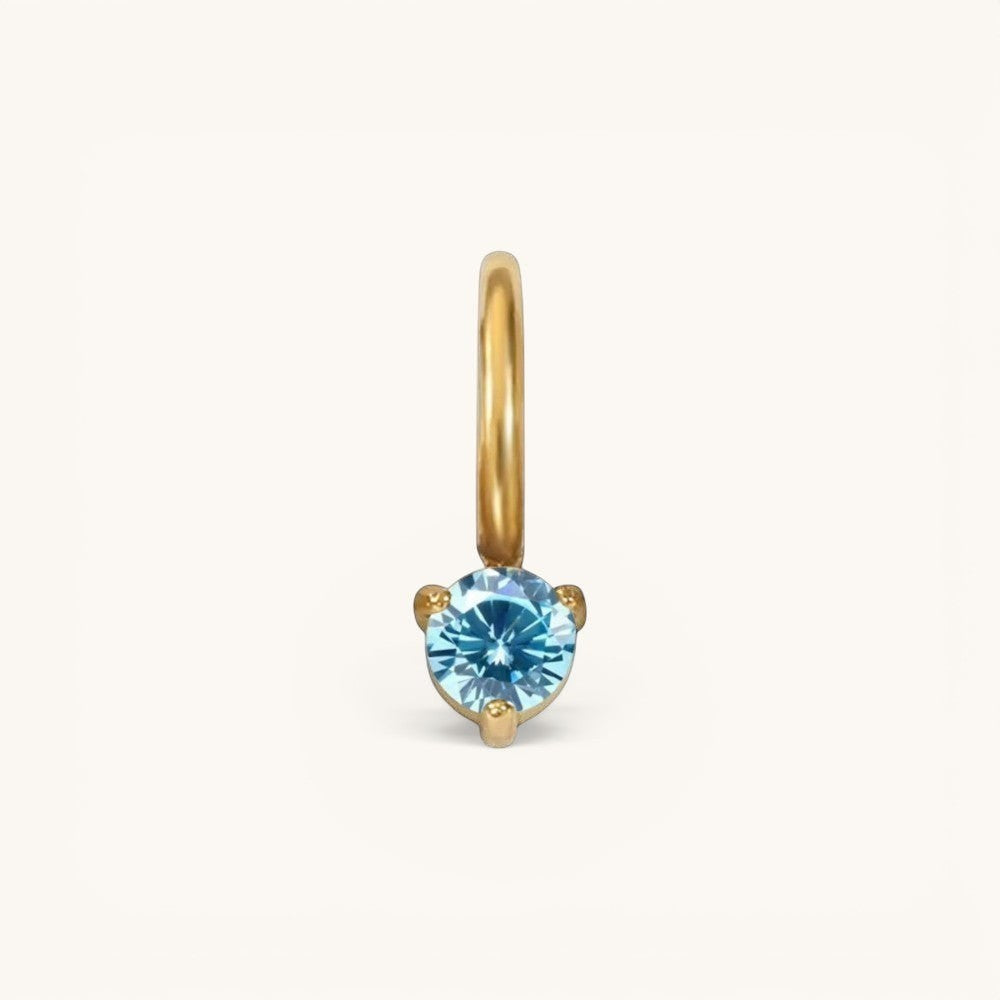 Nadare Co. mini gold birthstone charm featuring a round, brilliant-cut blue gemstone in a three-prong setting.