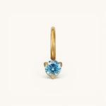 Nadare Co. mini gold birthstone charm featuring a round, brilliant-cut blue gemstone in a three-prong setting.