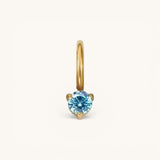 Nadare Co. mini gold birthstone charm featuring a round, brilliant-cut blue gemstone in a three-prong setting.