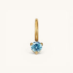 Nadare Co. mini gold birthstone charm featuring a round, brilliant-cut blue gemstone in a three-prong setting.