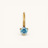 Nadare Co. mini gold birthstone charm featuring a round, brilliant-cut blue gemstone in a three-prong setting.