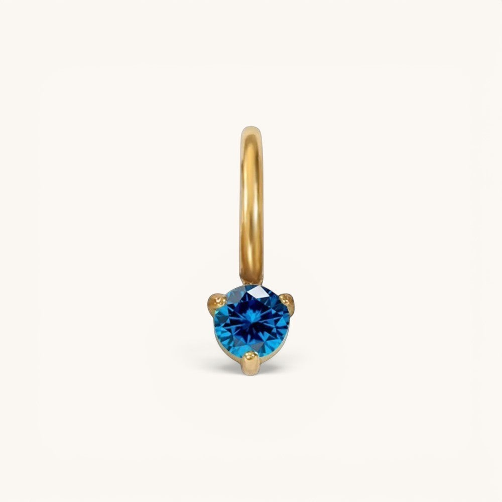 Nadare Co. mini birthstone charm featuring a round-cut blue gemstone set in polished gold on a small hoop.
