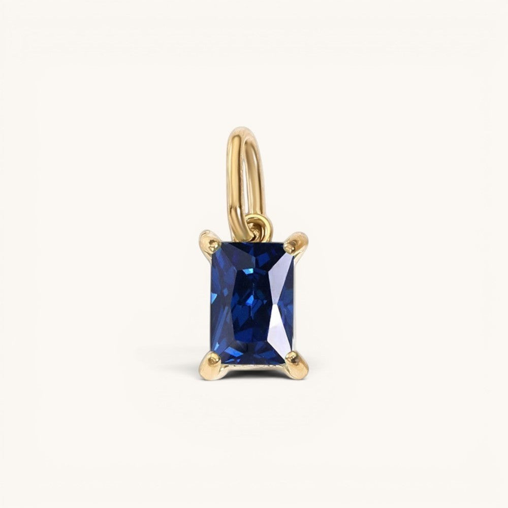 Nadare Co. rectangle birthstone charm featuring a deep blue sapphire-style gemstone set in polished yellow gold.