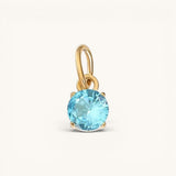 Nadare Co. round birthstone charm featuring a brilliant-cut light blue gemstone set in polished gold.