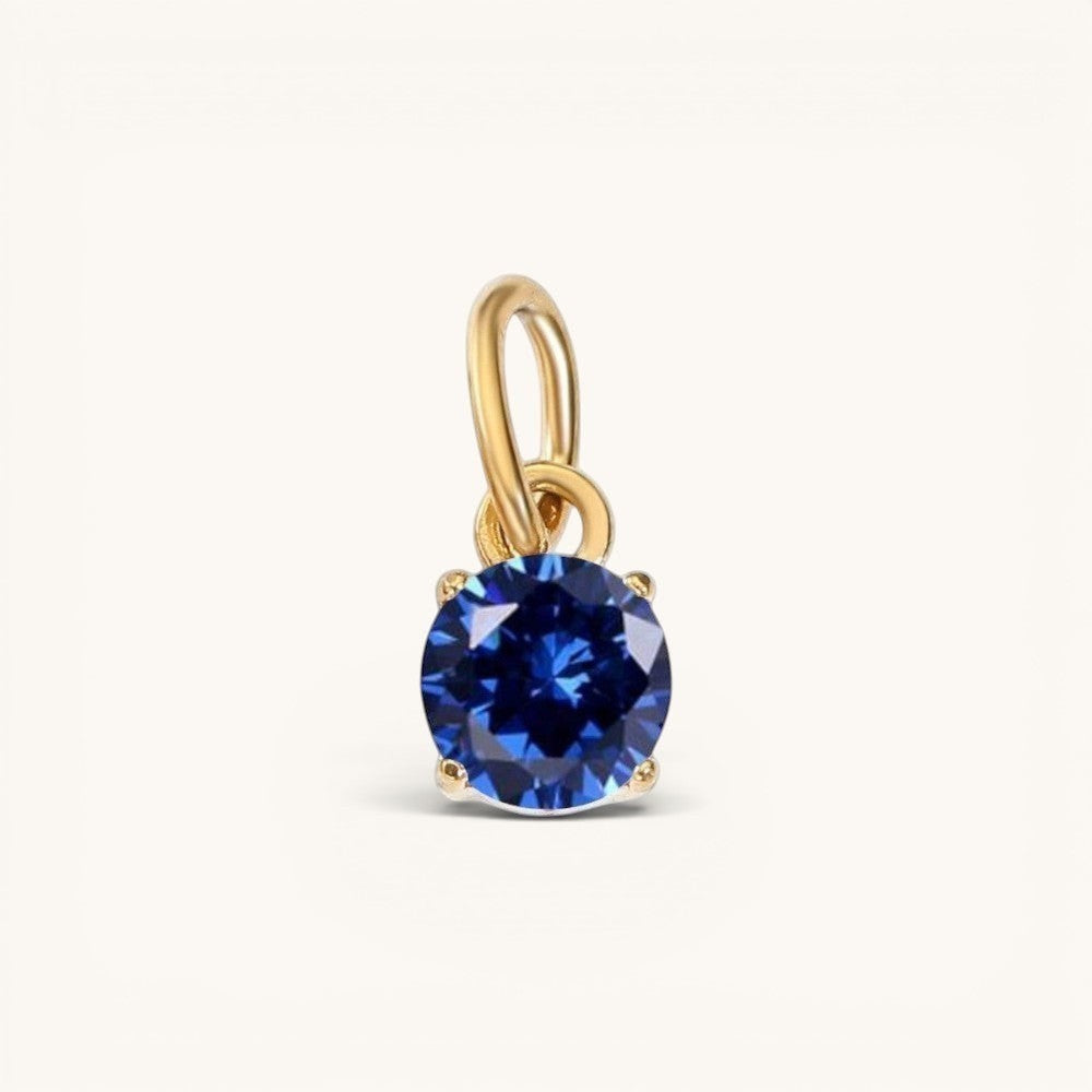 Nadare Co. round birthstone charm featuring a deep blue cubic zirconia stone set in 14k gold plated stainless steel.