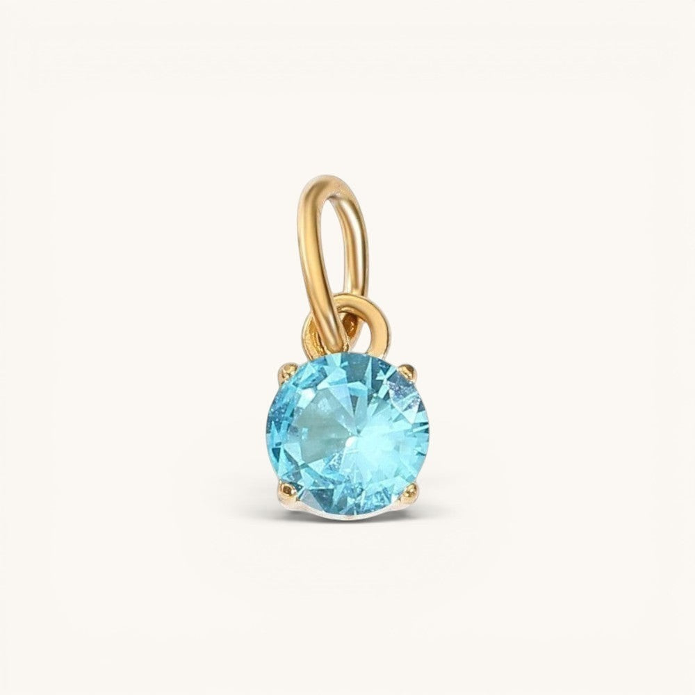 Nadare Co. round birthstone charm featuring a sparkling light blue cubic zirconia in 14k gold-plated stainless steel.