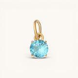 Nadare Co. round birthstone charm featuring a sparkling light blue cubic zirconia in 14k gold-plated stainless steel.