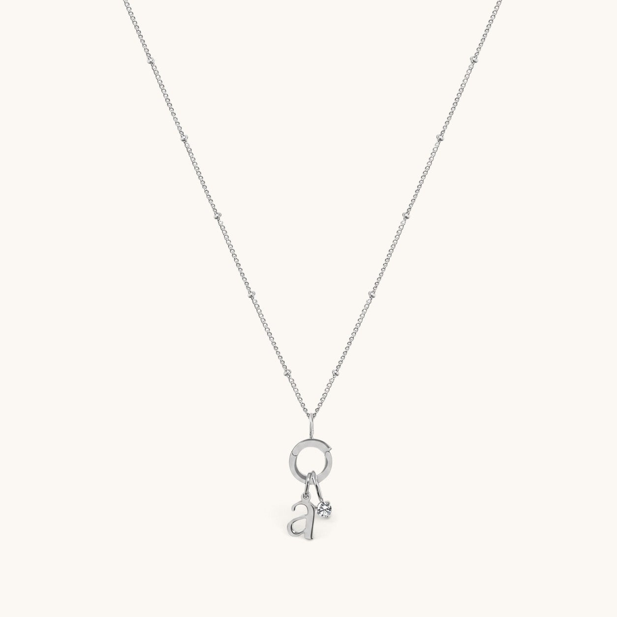 Nadare Co. silver necklace featuring a delicate chain with a circular charm, a lowercase letter a, and a birthstone.