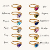 Nadare Co. Vela Birthstone Ring collection featuring 12 gold stainless steel open bands with trillion-cut gemstones.